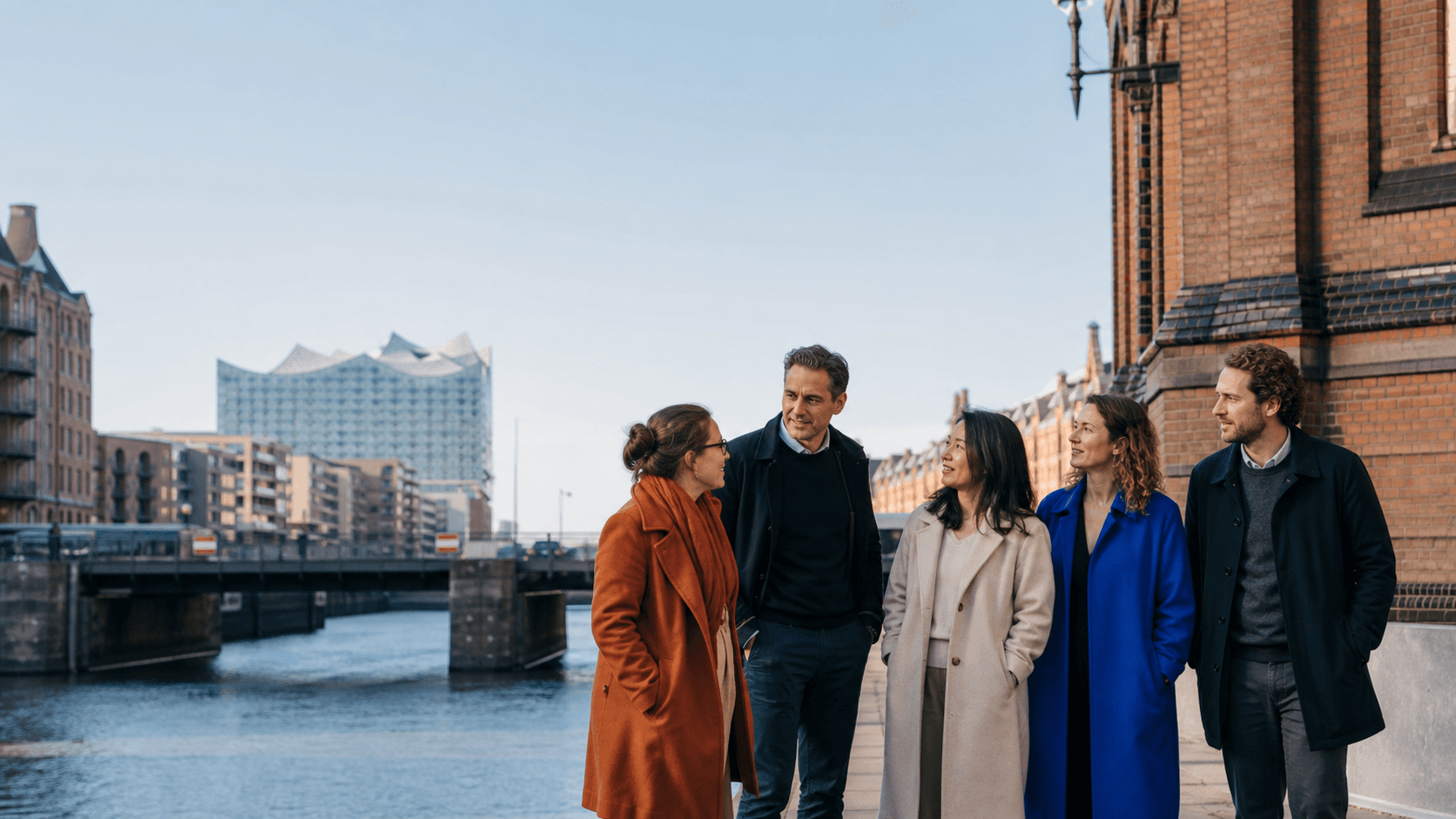 Ein vielfältiges Dudoxx-Team an der Hamburger Speicherstadt mit der Elbphilharmonie im Hintergrund