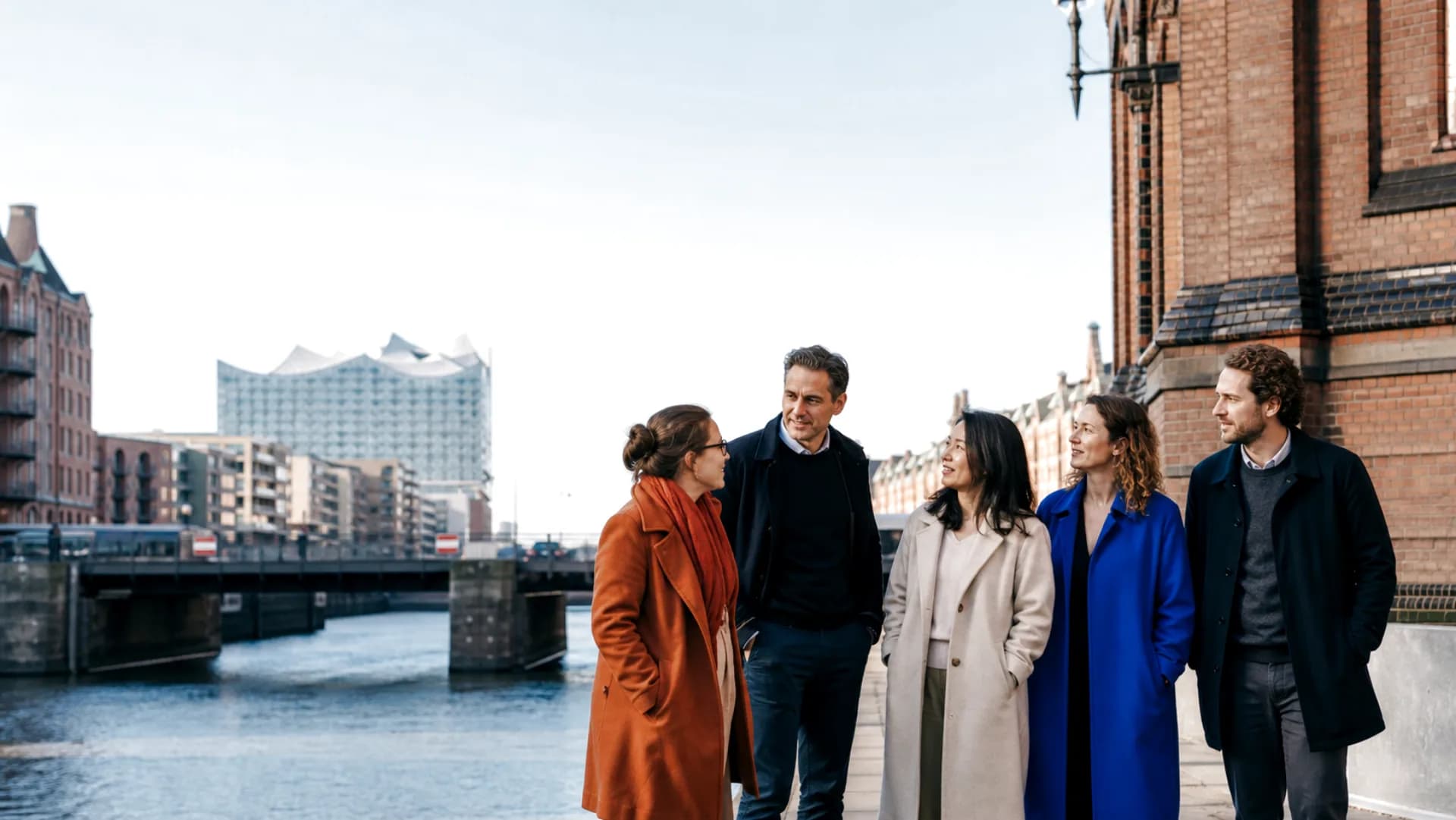 Un equipo diverso de Dudoxx junto a la Speicherstadt de Hamburgo con la Elbphilharmonie al fondo
